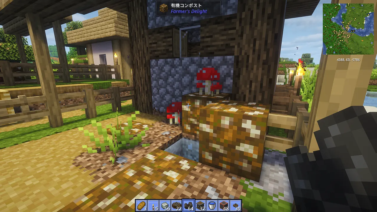 村の耕地で栽培されているトマトの成長風景。Farmer's Delight Modで追加されたトマトが支柱に沿って育っており、背後にはのどかな村の家々が広がる農村の景色。