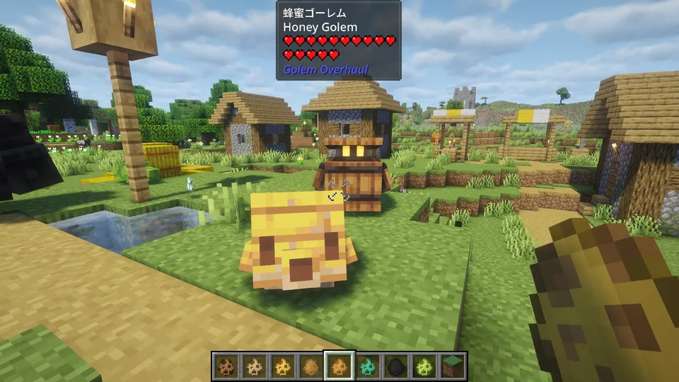 Golem Overhaul Modの「蜂蜜ゴーレム」。ミツバチの巣箱やハチミツの塊を思わせる、黄色と茶色の四角い体が特徴。つぶらな瞳を持ち、村の風景に溶け込むマスコットのようなサイズ感。