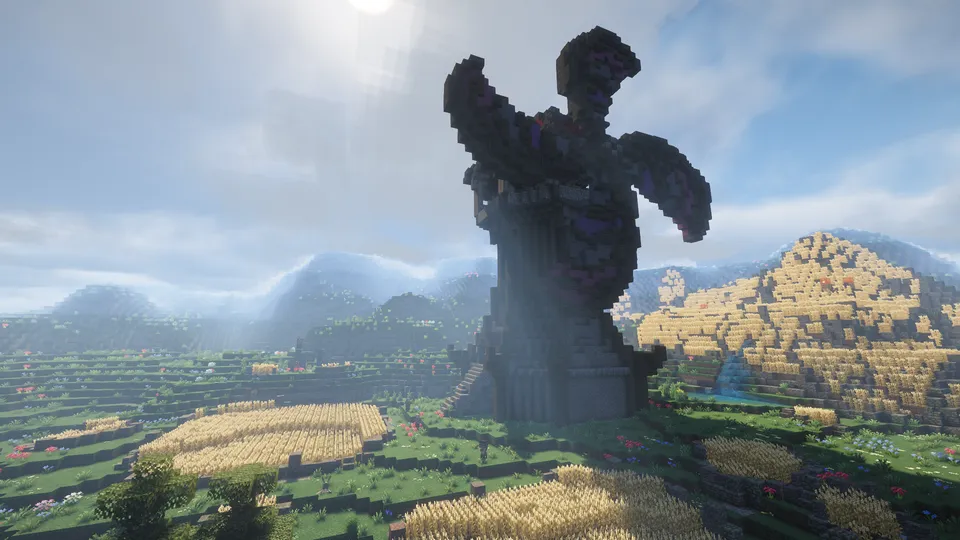 平原に建つ巨大な風車と、その周囲に広がる広大な麦畑の風景。遠くの山々に霧がかかる幻想的なライティングの中で、大規模な農業と中世の技術が融合した壮大な景色が広がっています。